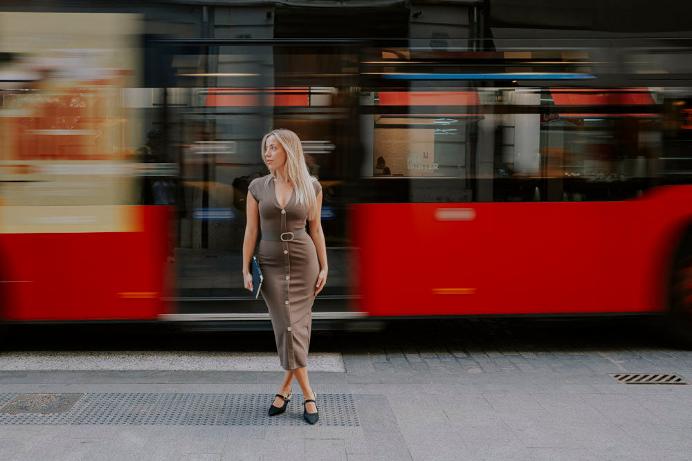 Mujer con vestido midi y zapatos planos cruzando una calle con un tranvía al fondo